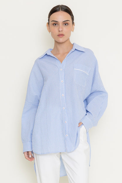 Model wearing oversized blue pinstripe button-up shirt with curved hem